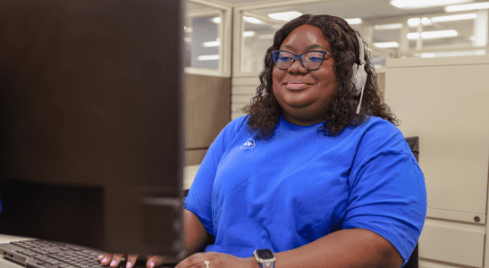 Employee smiling at her computer and wearing a headset.