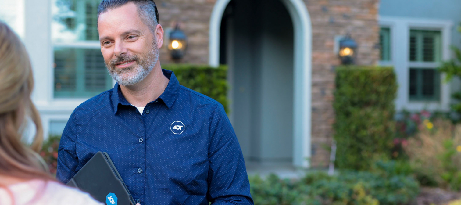 A male ADT Sales Rep stands outside a home talking with the female homeowner.