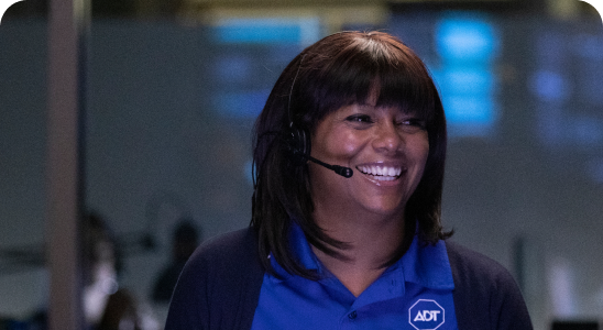 A female ADT Inside Sales employee wearing a microphone headset smiles as she talks with a customer.